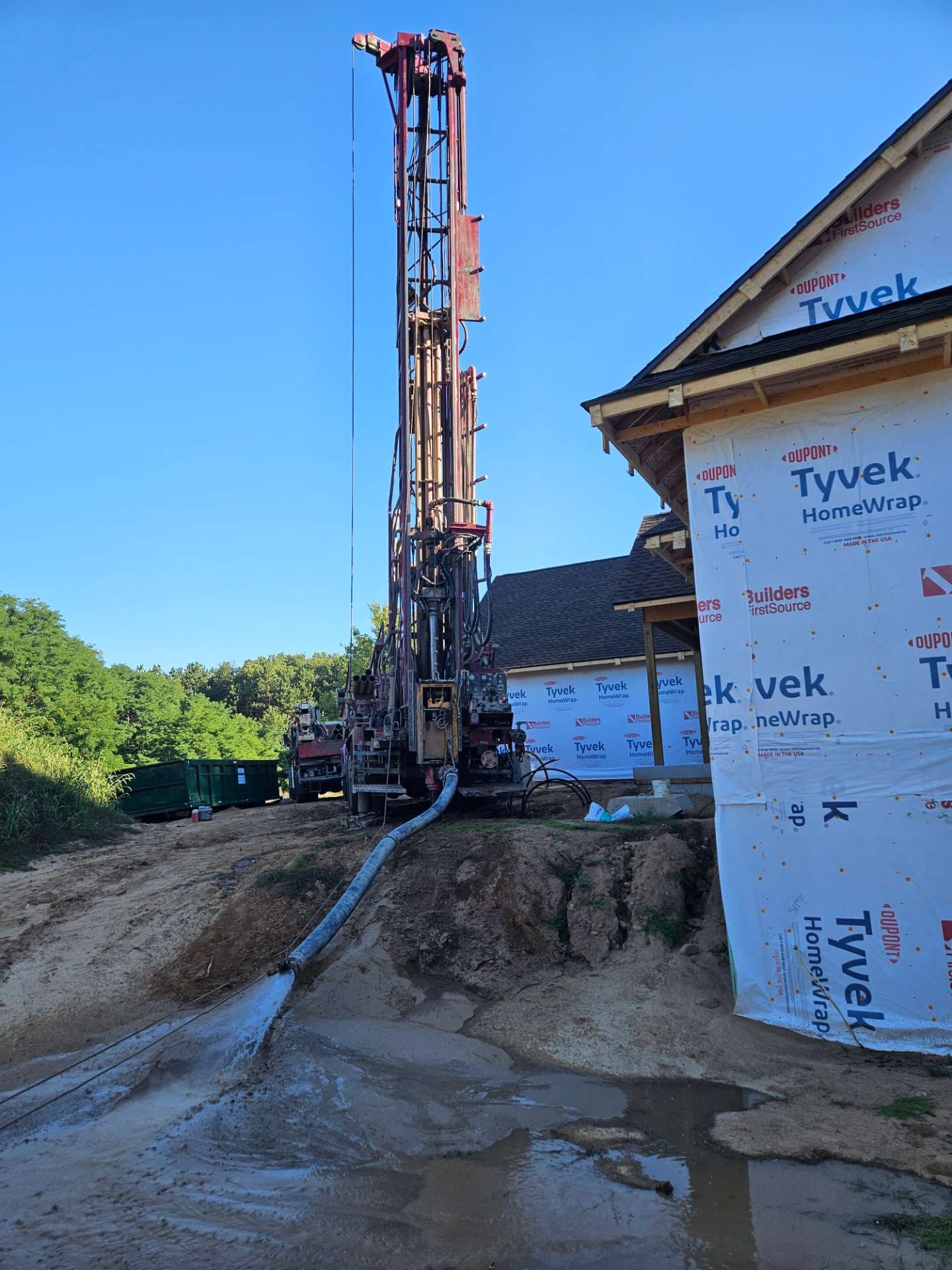 A Sam's Well Drilling rig drilling a residential well — mud, trench and all